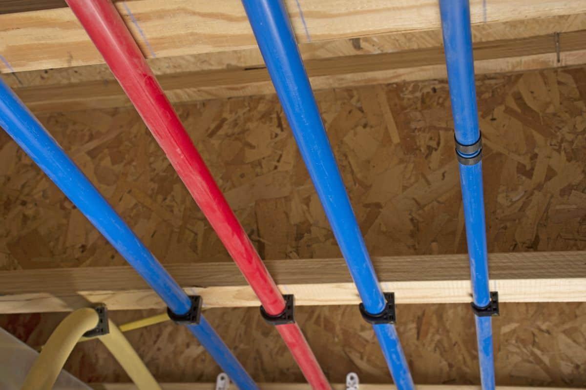 PEX and drain pipes attached to the basement ceiling of a home, angled view.