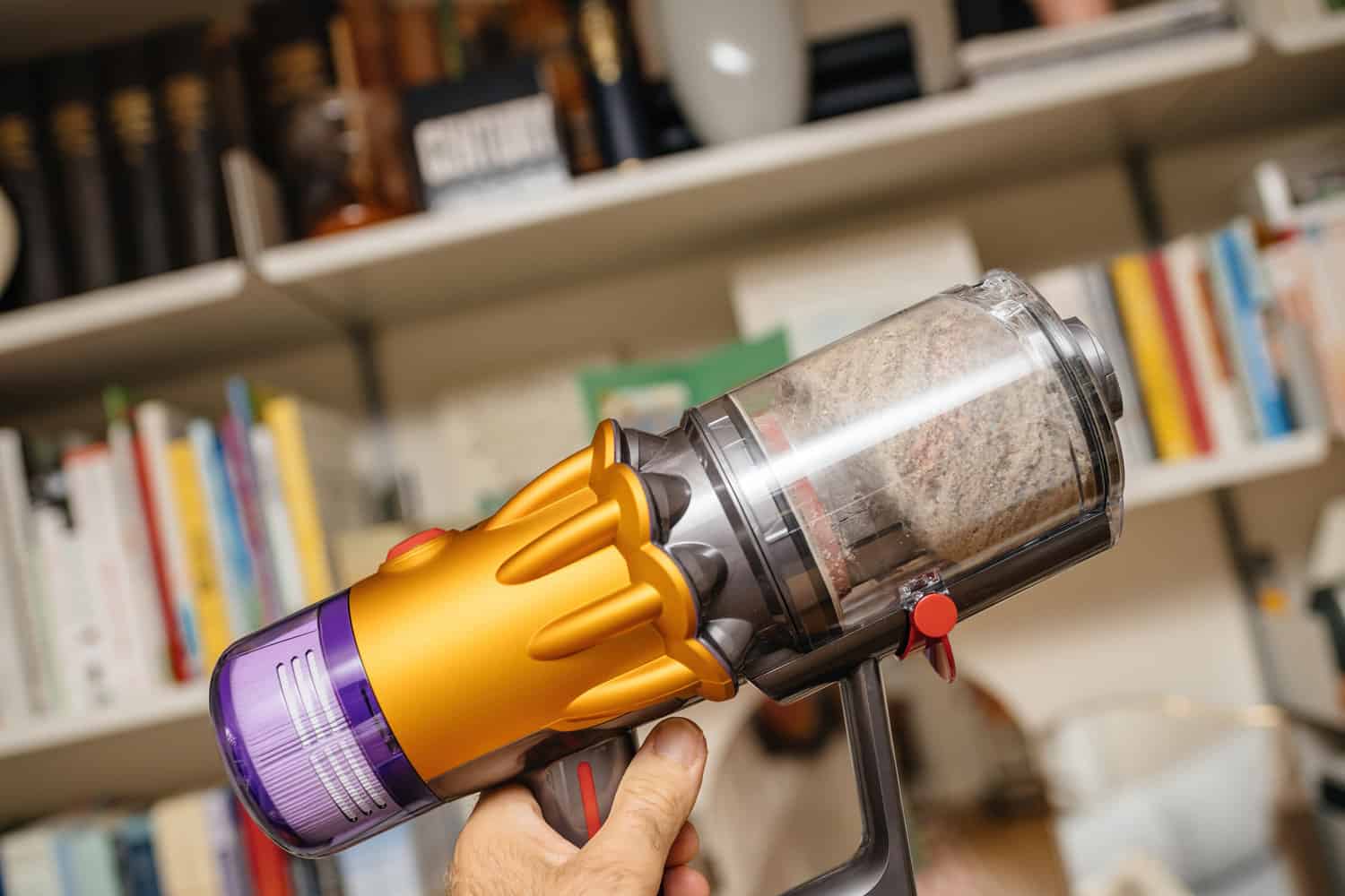 POV male hand holding new cordless vacuum cleaner by Dyson V12 with filled bin multiple dust particle, hair and other debris found in house
