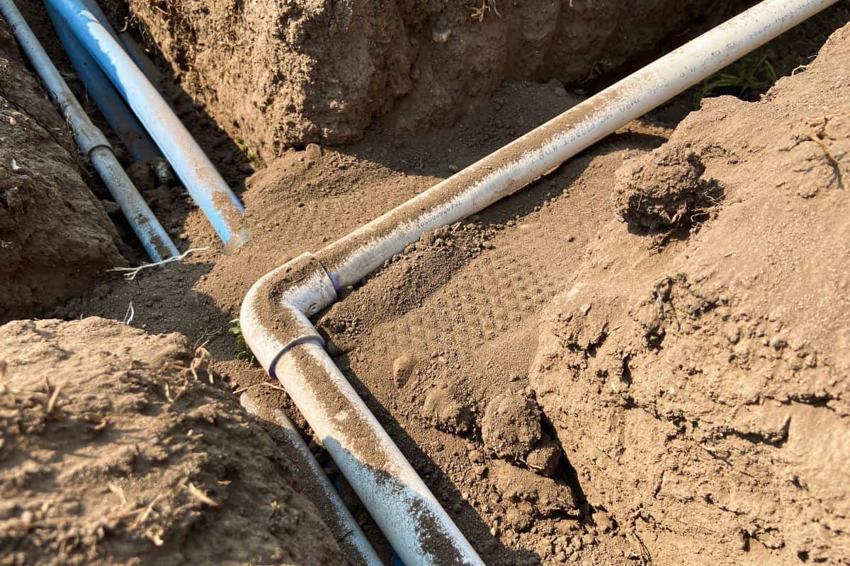 PVC pipe, blue pipe, and electrical conduit running through trench filled with dirt