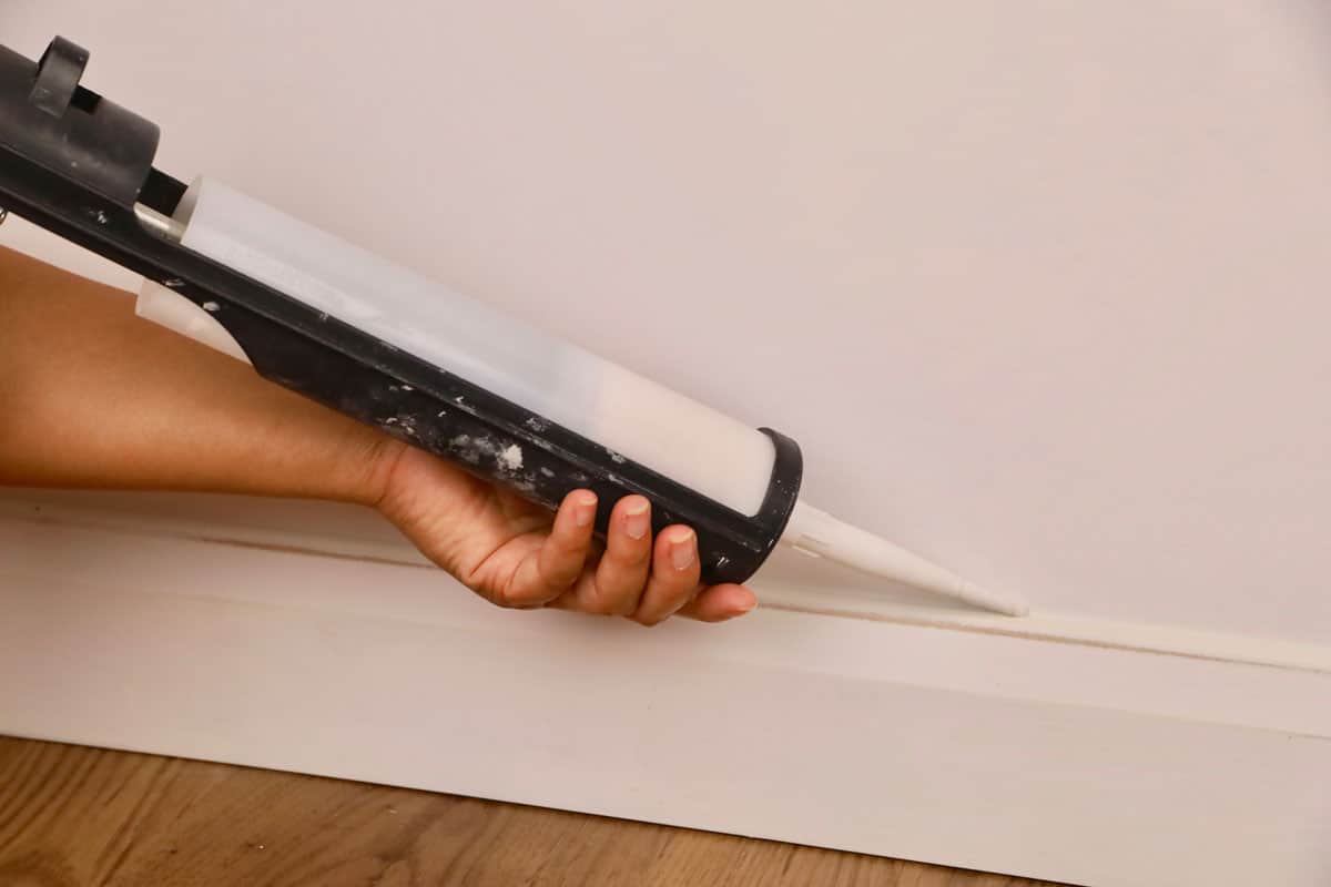 a female contractor using a mastic gun to seal a baseboard