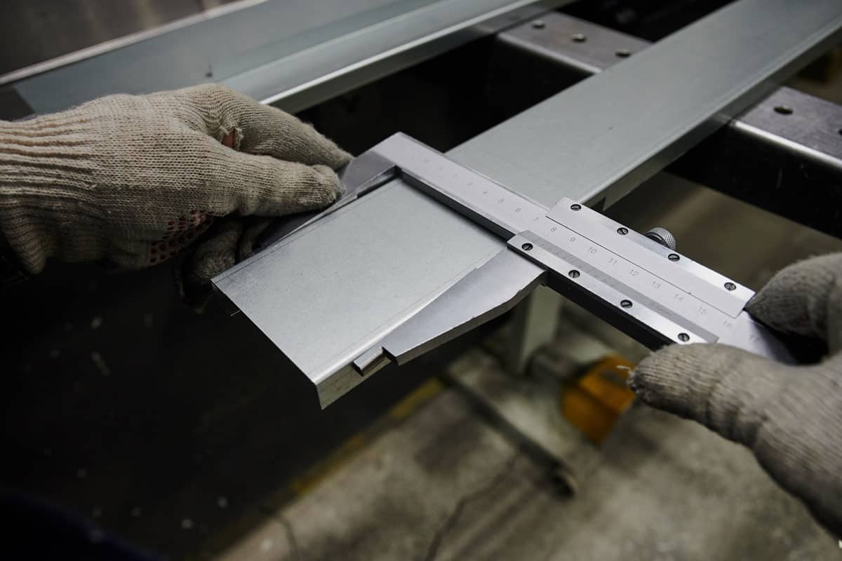 A specialist at the factory measures the accuracy of bending of metal sheet used as a cover for an industrial radiato