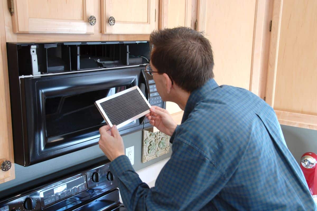 Man replacing the filter in a microwave in the kitchen of a modern home.