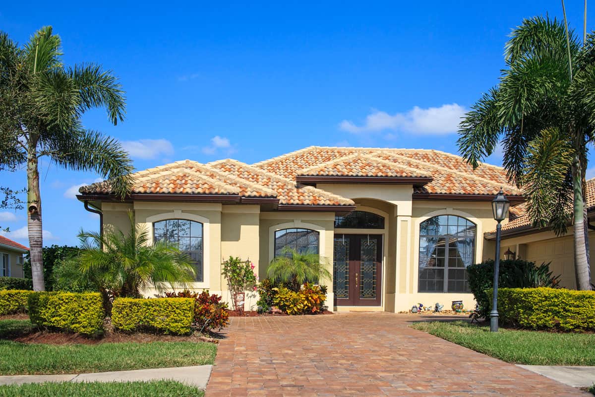New contemporary Florida-style home with driveway, tiled roof, palm trees, shrubbery and tropical foliage