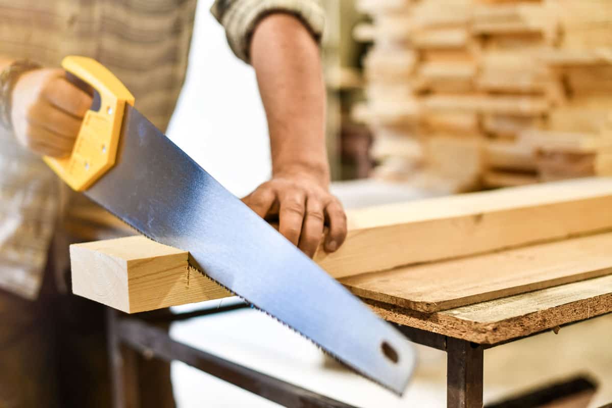 Worker hands use a wood cutter or saw on wooden board.