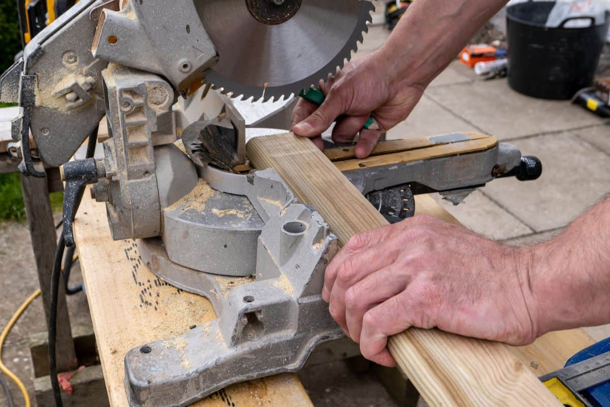 A joiner carefully holding a length of wood in an electric circular saw