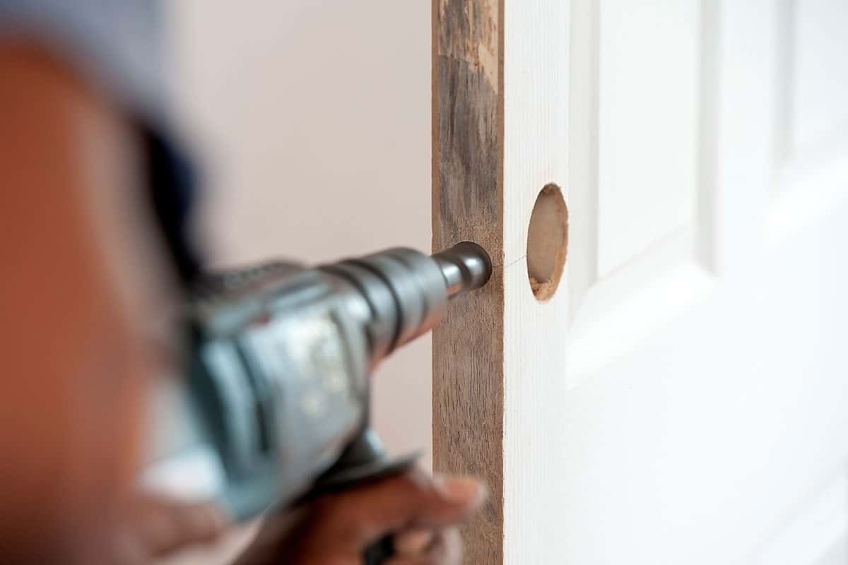 Cabinet-maker hands drilling a wooden door using electric drill on the working place in home