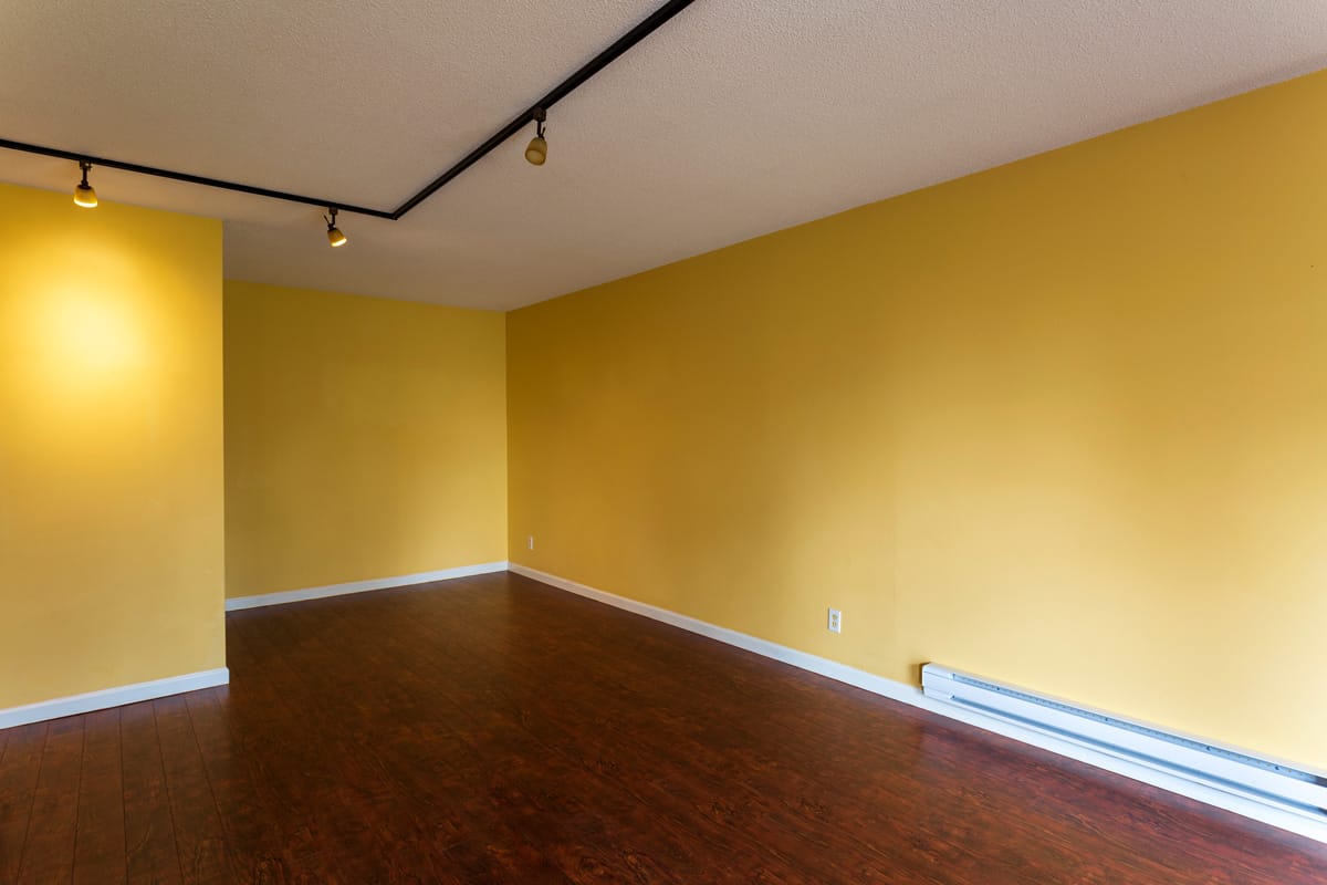 Interior of an empty apartment with hardwood flooring, white baseboard and tan ceiling with a baseboard heater