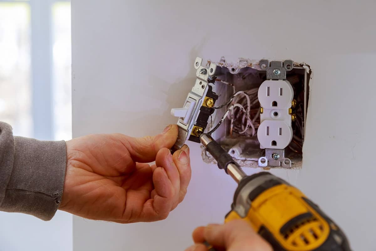 NEC - The hands of an electrician installing a power switch to the electrical junction box