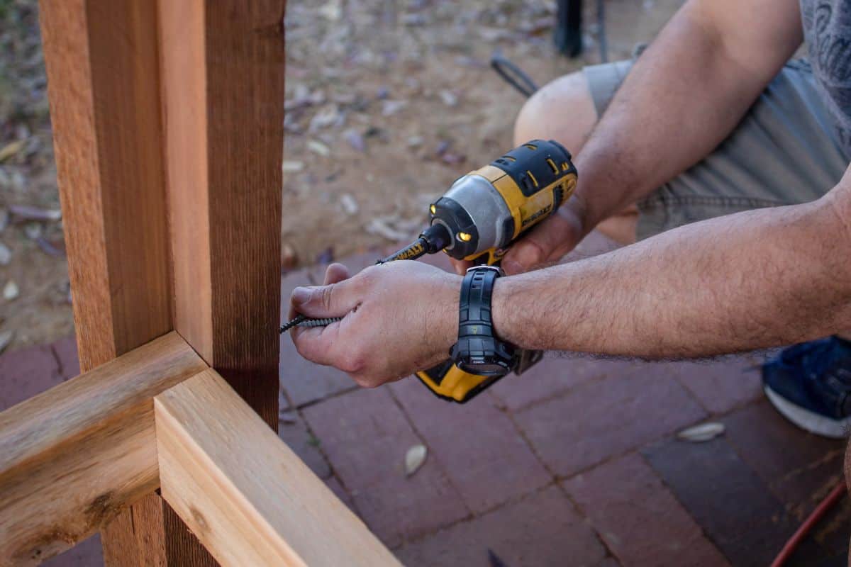 Closeup of man's hands as he uses a cordless electric power screwdriver to place screws into a wooden post