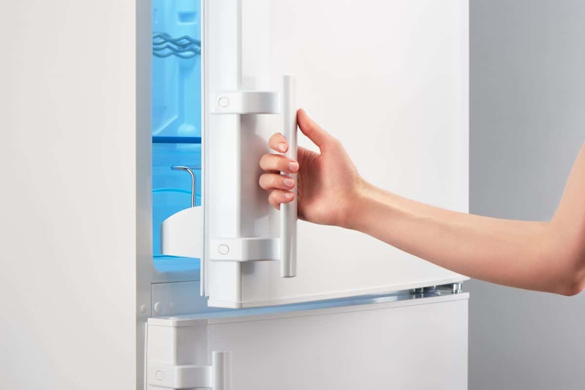 Female hand opening white refrigerator door on gray background