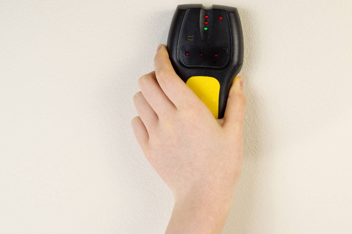 Hand holding stud finder against interior home white wall