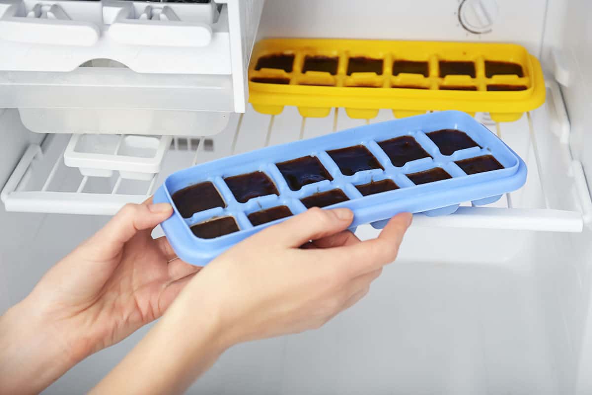 Woman taking tray with coffee ice cubes out of fridge