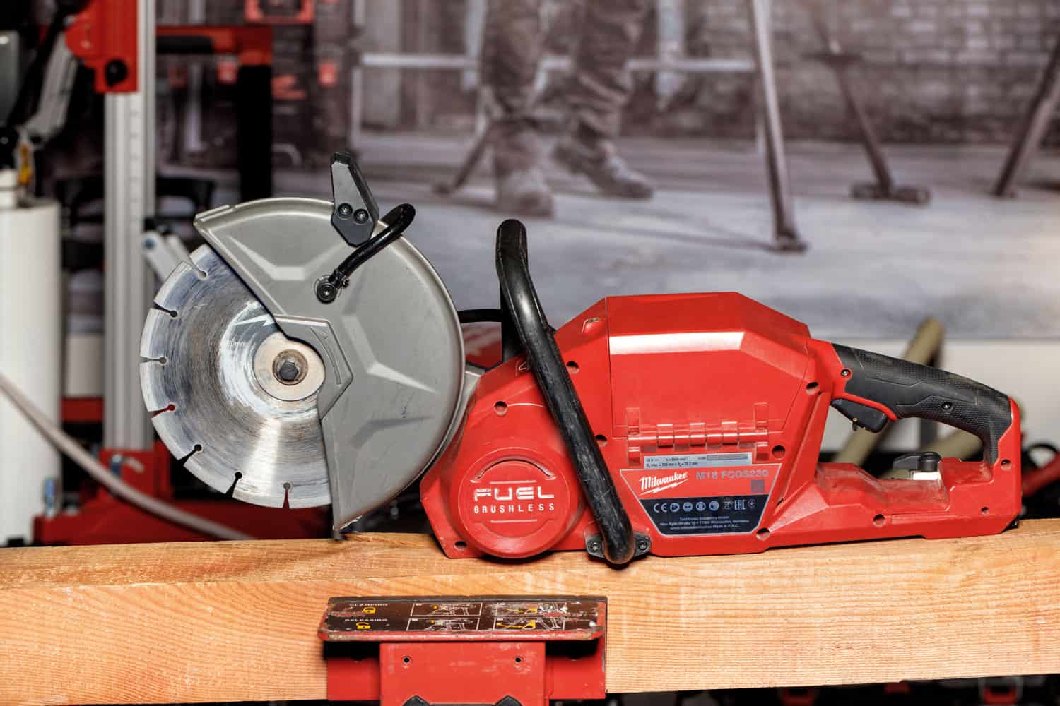 A portable red Milwaukee electric cutter with a diamond cutting wheel on a wooden beam and a blurred background.