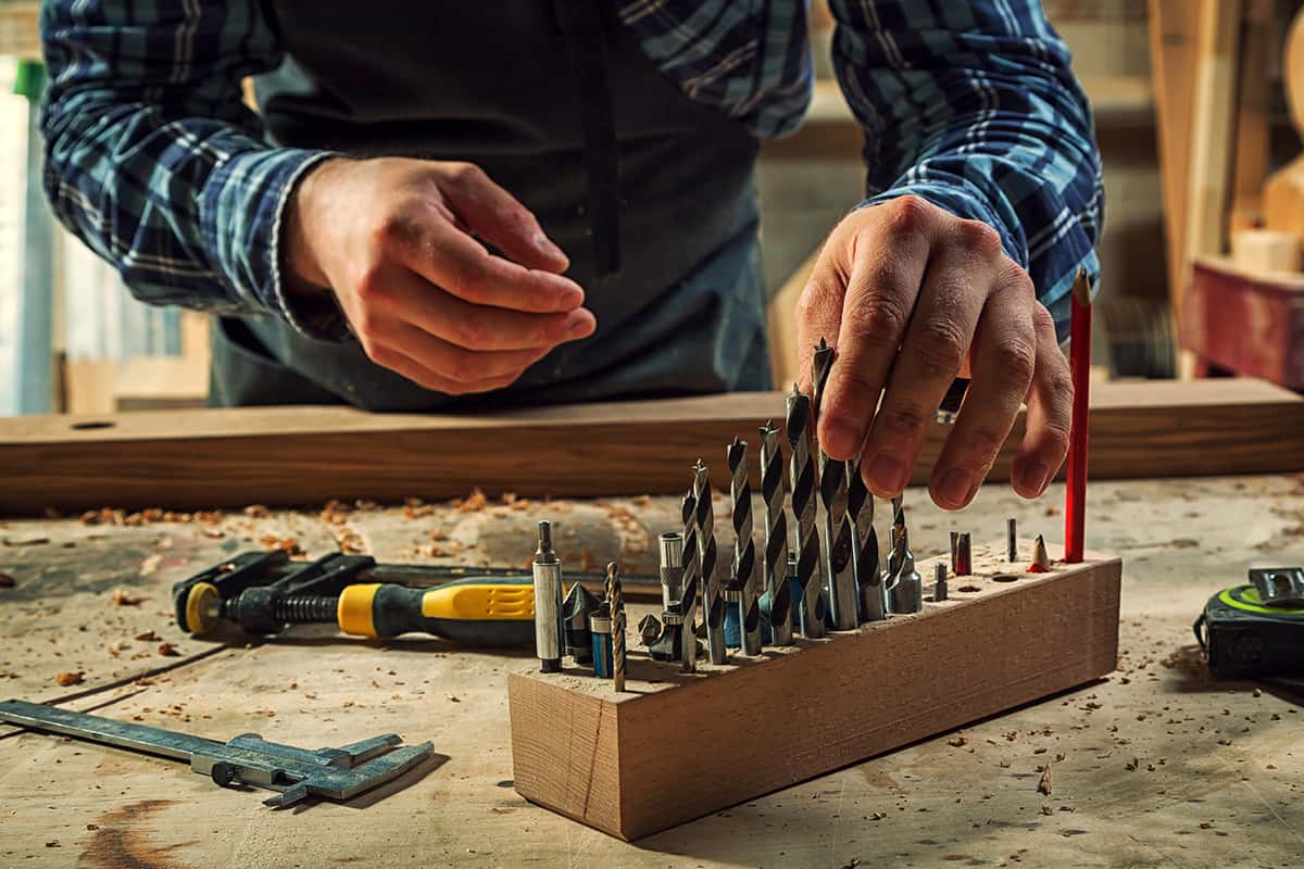 Carpenter chooses a drill for drilling a wooden block