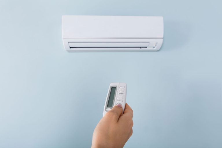 Hand holding the remote control of newly installed white air conditioner, How To Check Refrigerant Level In A Split AC [Step By Step Guide]