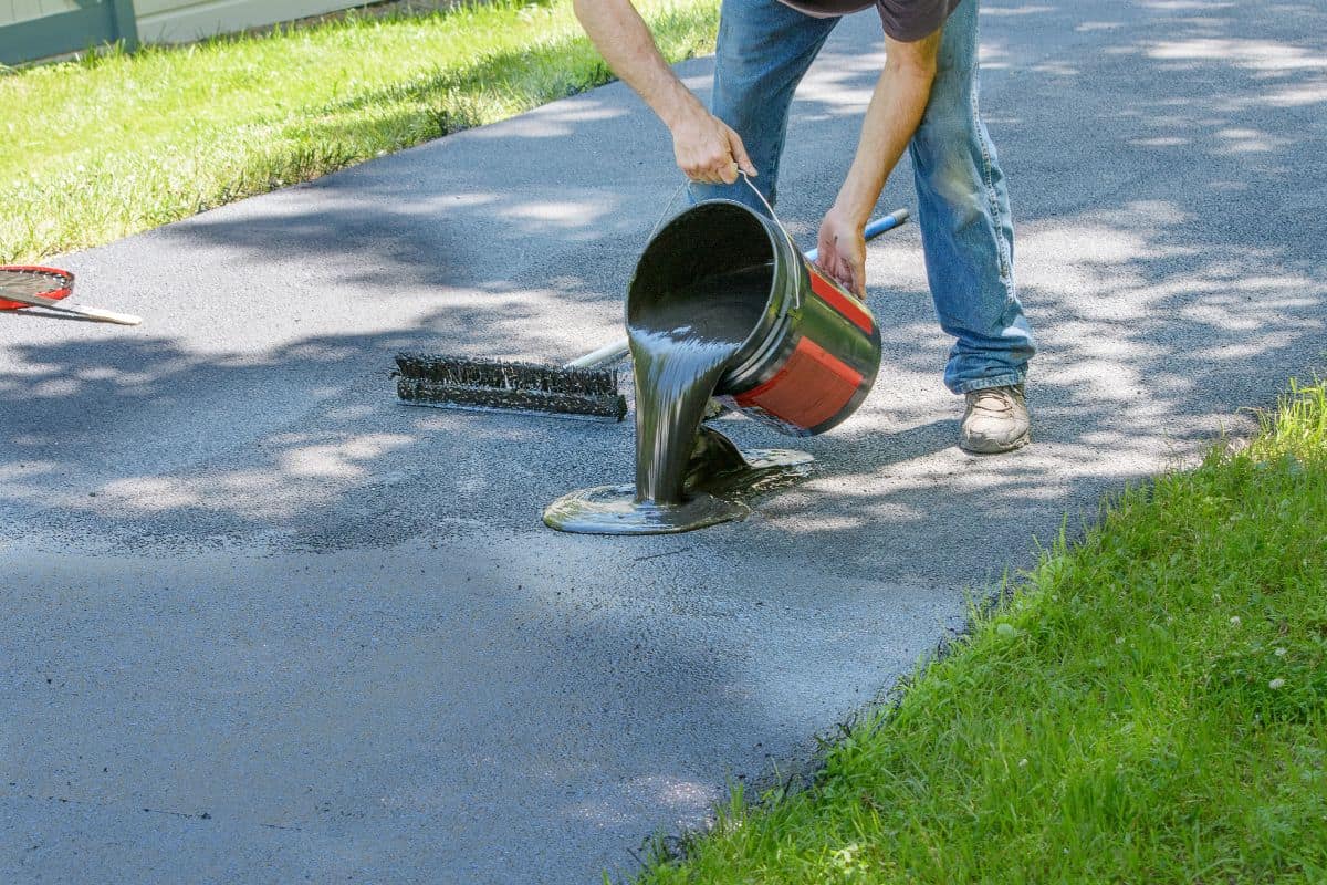 Do it yourself home maintenance. Driveway resealing repair. Homeowner pours blacktop sealant onto driveway