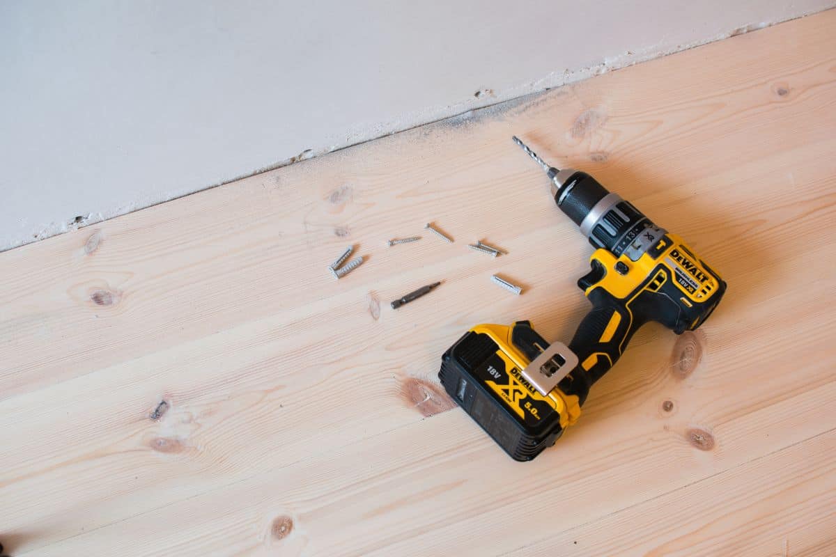  Drilling a hole in a concrete wall using a cordless Dewalt drill, on a background of a wooden floor.