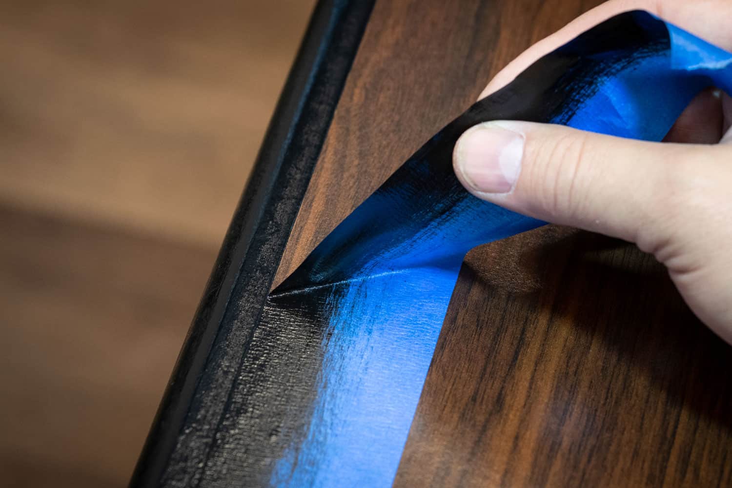 Hand removing blue painter's tape from edge of refinished furniture paint job. 