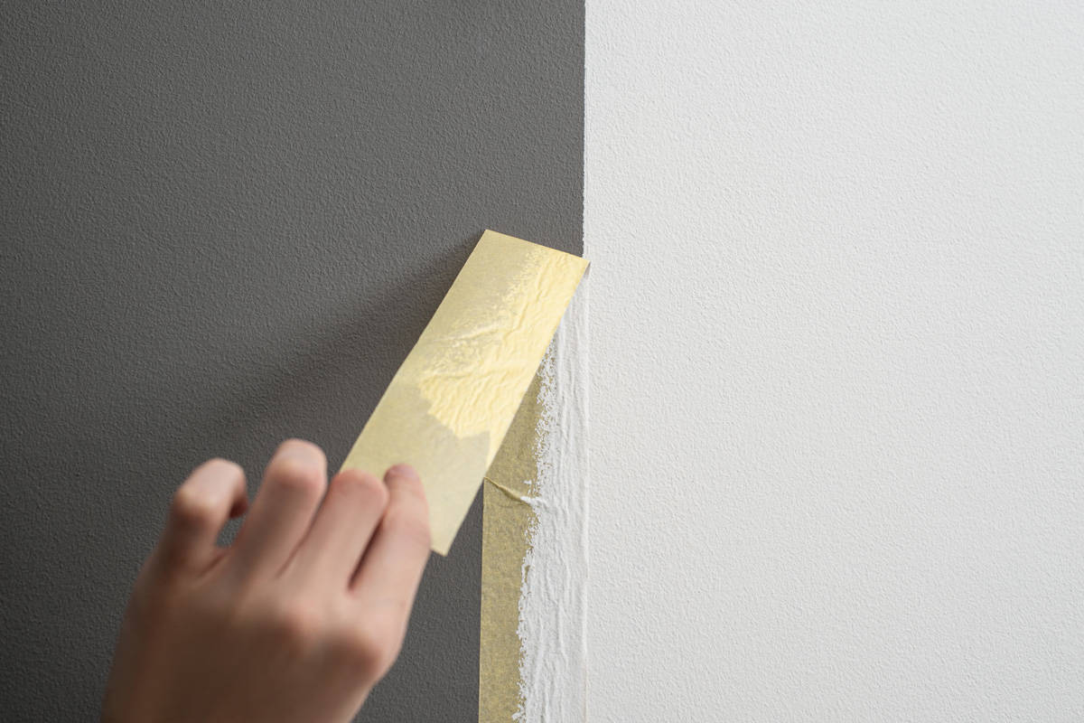 Hand taking off masking tape from the wall after painting. 
