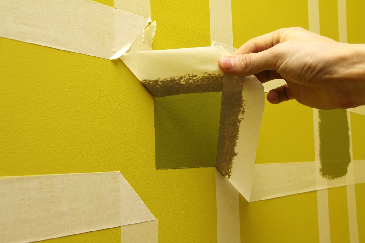 worker man removing masking tape from painting wall