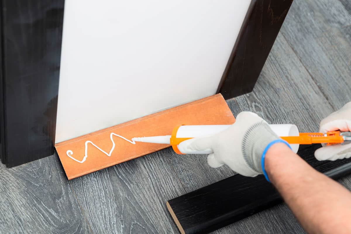 Handyman is putting a silicon glue from tube on a wooden baseboard before attaching it to the wall