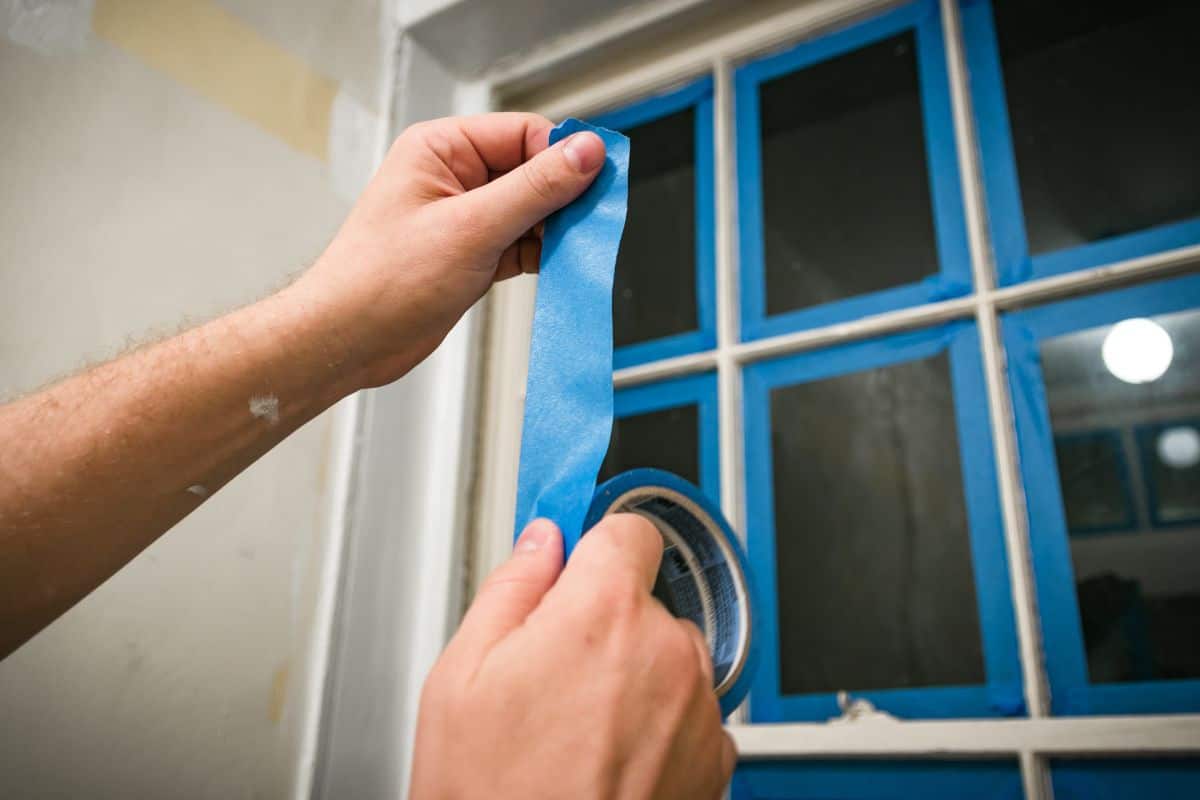Prepping a window for painting - taping off glass with blue painter's tape.