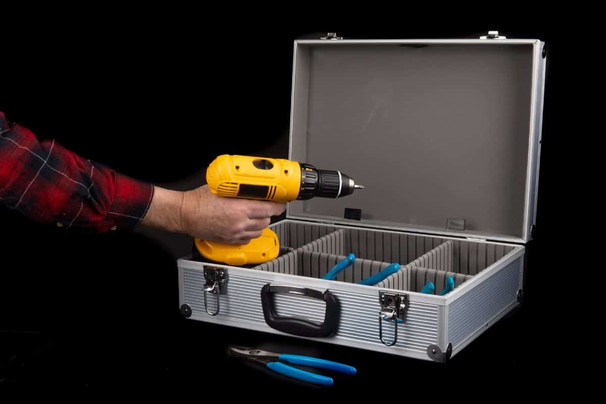 a worker in a red plaid shirt removes an electric drill from an aluminum case isolated on black