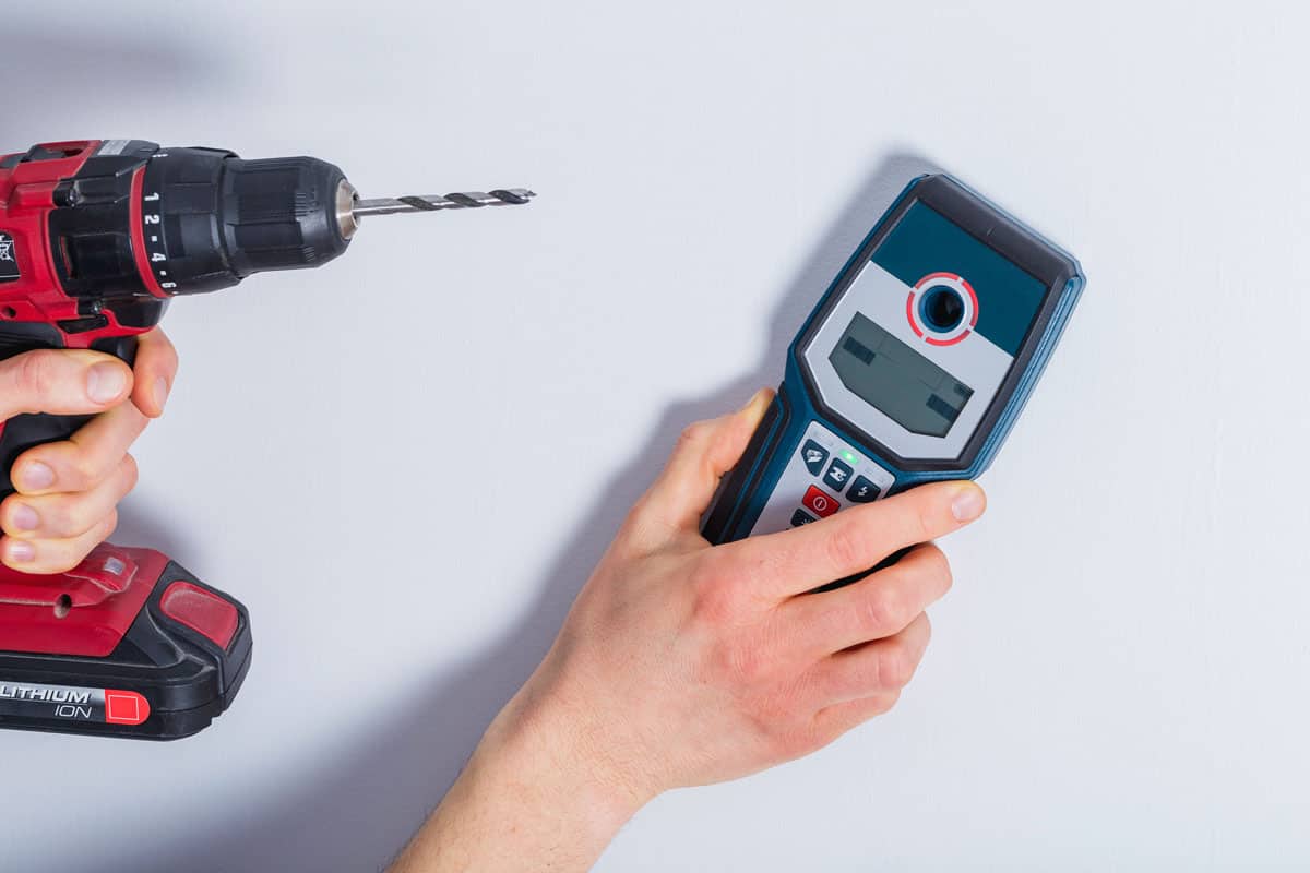 man hand scanning wall by cable scanner and holding a drill
