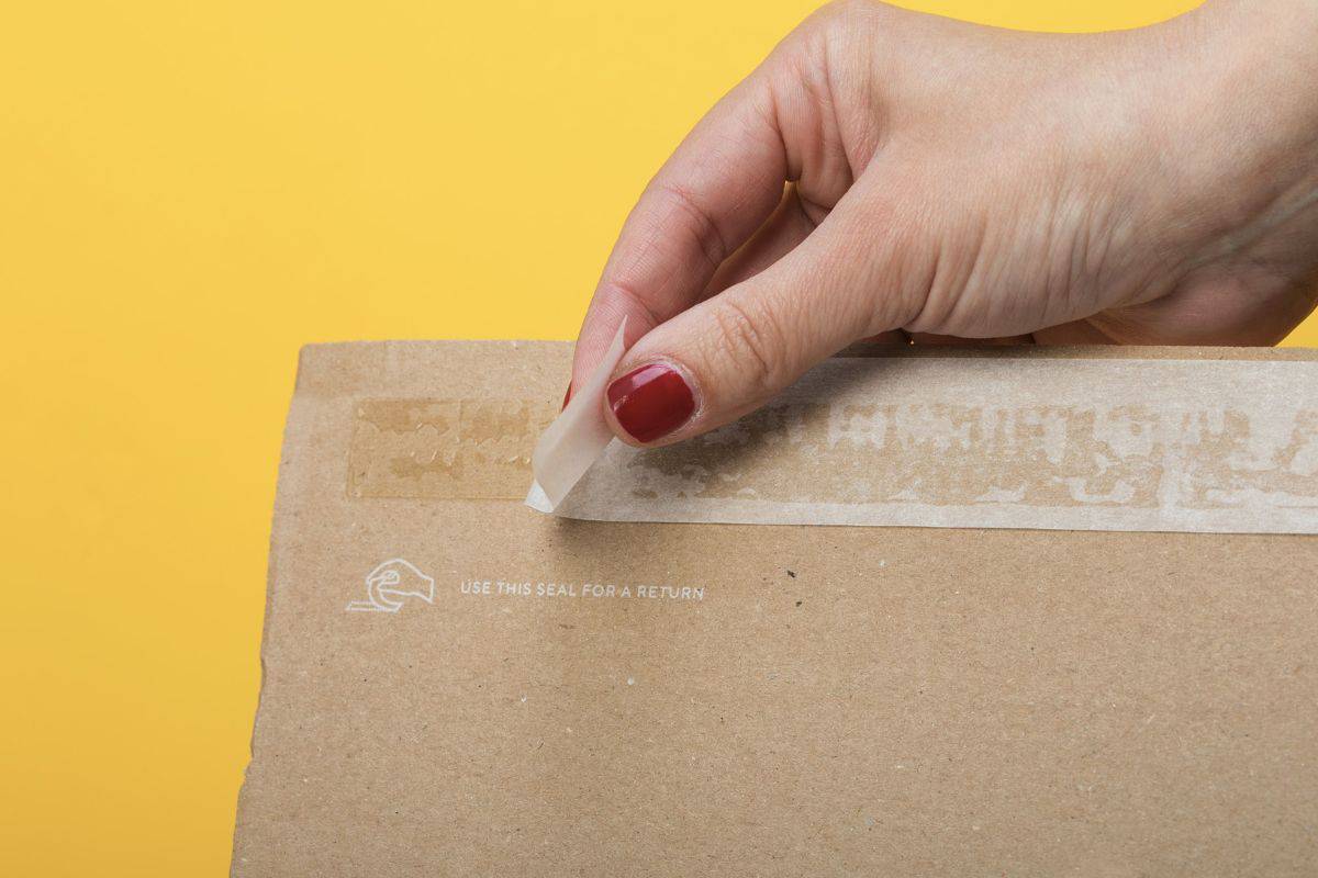 Resealing a package for ecommerce products, fashion items returning. Sticky self adhesive sealing tape on corrugated cardboard box