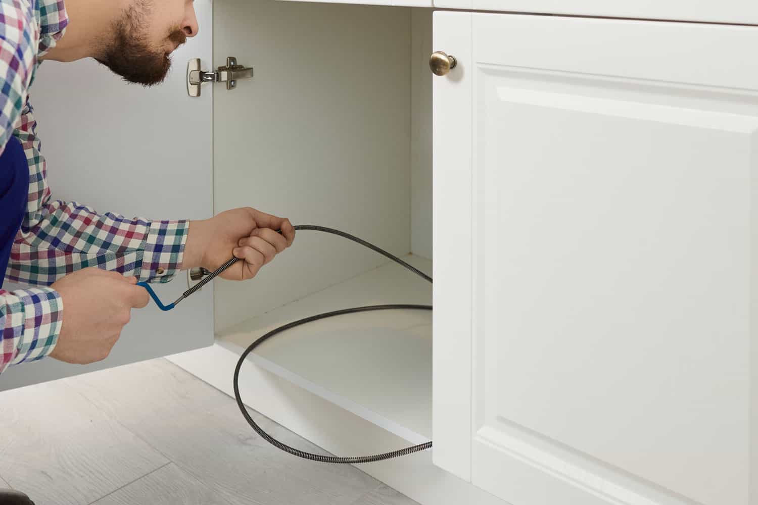 Plumber using drain snake to the kitchen sink
